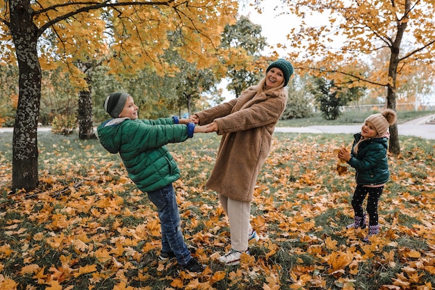 Famille heureuse marchant dans un parc ensoleillé et jette des feuilles d'érable orange mère avec des enfants profitant du temps d'automne à l'extérieur