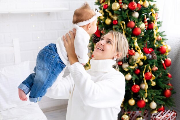 Une famille heureuse de mère et d'enfant l'enfant joue à la maison pour les vacances de Noël Les vacances du Nouvel An Un bébé avec sa mère dans une pièce décorée de façon festive avec un arbre de Noël