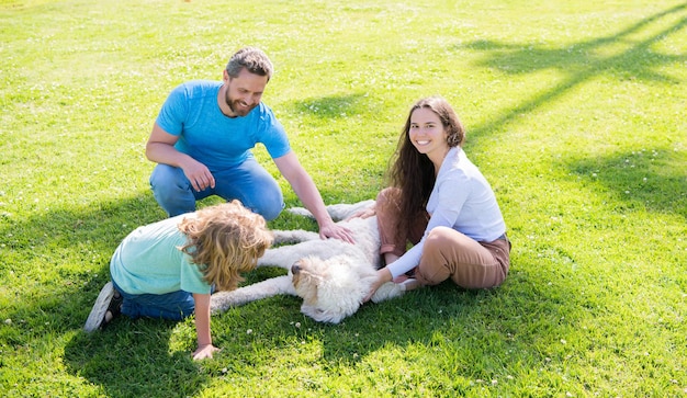 Famille heureuse de mère papa et fils enfant jouant avec un chien de compagnie dans l'adoption de l'herbe verte du parc d'été