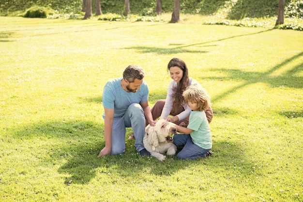 Famille heureuse de mère papa et fils enfant jouant avec un chien de compagnie dans l'été de l'herbe verte du parc