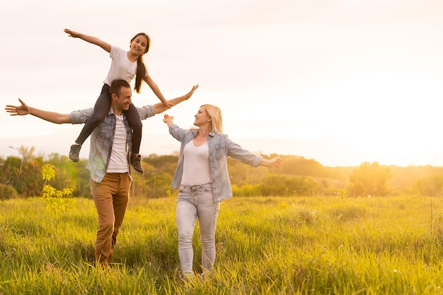 Famille heureuse : mère, père, enfant fille sur la nature au coucher du soleil.