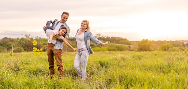 Famille heureuse : mère, père, enfant fille sur la nature au coucher du soleil.