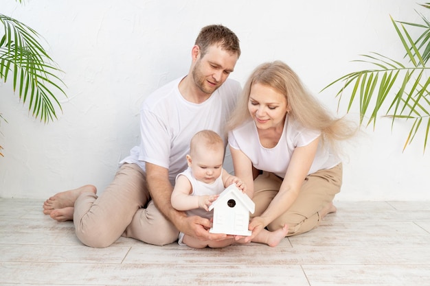 Famille heureuse une mère et un père tiennent une maquette d'une maison, la montrant à leur fils en bas âge, le concept de logement ou une hypothèque pour une jeune famille