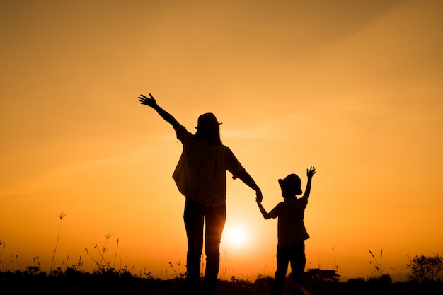 famille heureuse. Une mère et son fils jouent dans les champs d&#39;herbe en plein air à la silhouette du soir