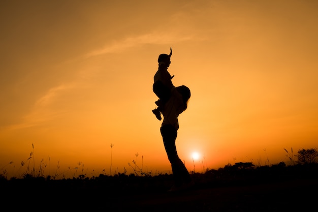 famille heureuse. Une mère et son fils jouent dans les champs d&#39;herbe en plein air à la silhouette du soir