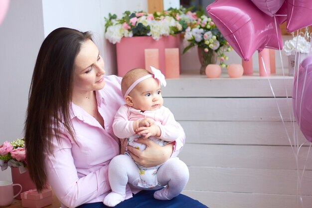 Famille heureuse. Mère avec son petit bébé dans une salle de vie intérieure lumineuse. Célébration de la fête des mères avec des cadeaux et des fleurs