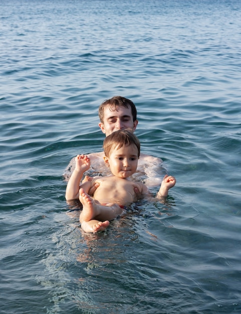 Photo famille heureuse et mode de vie sain. un jeune père apprend à un enfant à nager dans la mer