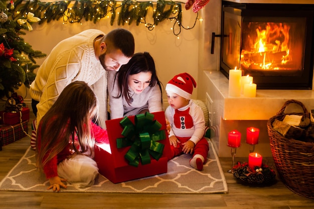 Une famille heureuse ouvre une boîte-cadeau d'éclairage de Noël près de l'arbre de Noël. La famille célèbre Noël dans la nuit magique