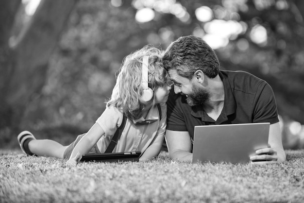 Une famille heureuse de papa et de fils utilise un ordinateur portable pour un appel vidéo ou une leçon écoute de la musique dans des écouteurs dans la parentalité du parc