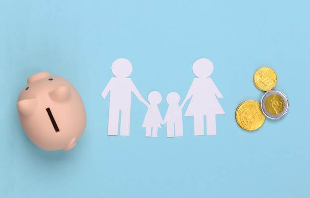 Famille heureuse de papier avec tirelire et pièces de monnaie sur bleu. Budget familial