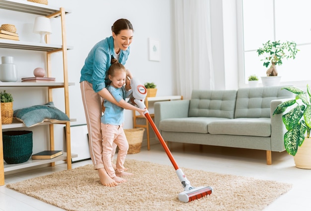 Famille heureuse passant l'aspirateur dans la chambre. Mère et fille faisant le ménage dans la maison.