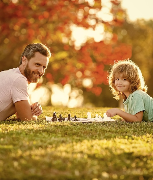 Famille heureuse de père homme et fils enfant jouant aux échecs sur l'herbe verte dans le cerveau extérieur du parc