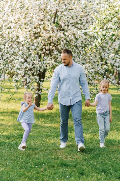 Famille heureuse Un père et ses deux filles se promènent dans le parc au printemps dans un jardin fleuri