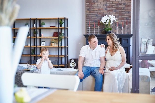 Une famille heureuse avec un petit enfant et une femme enceinte est assise sur le canapé du salon