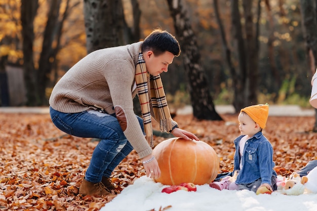 Famille heureuse avec petit enfant mignon dans le parc sur une feuille jaune avec grosse citrouille en automne