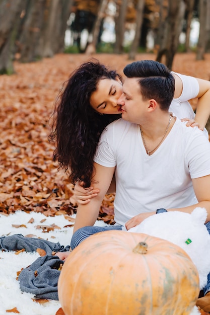 Famille heureuse avec petit enfant mignon dans le parc sur une feuille jaune avec grosse citrouille en automne