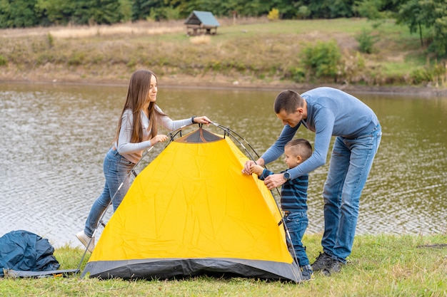 Famille heureuse avec petit fils mis en place une tente de camping. Enfance heureuse, voyage de camping avec les parents. Un enfant aide à monter une tente