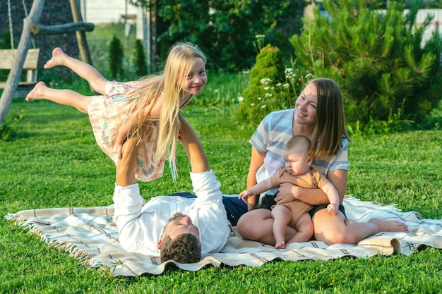 Famille heureuse et petits enfants sur une couverture dans l'herbe en été