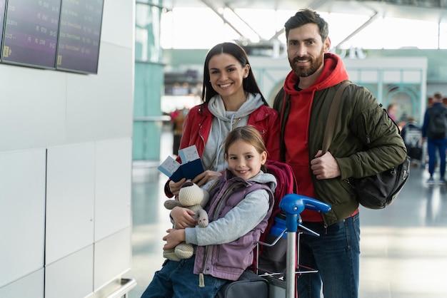 Photo famille heureuse posant devant la caméra avec des valises à l'aéroport. mère, père et fille regardant la caméra avec des sourires de plaisir