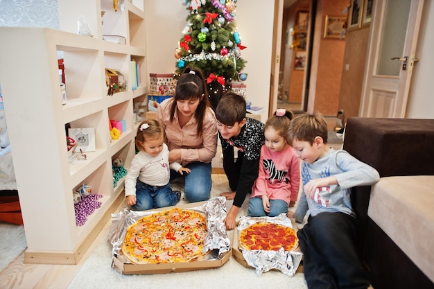 Famille heureuse avec quatre enfants mangeant de la pizza à la maison.