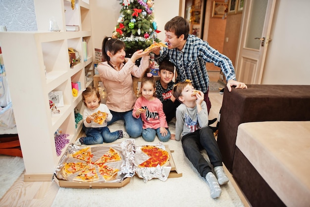 Famille heureuse avec quatre enfants mangeant de la pizza à la maison.