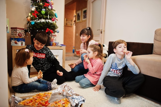 Famille heureuse avec quatre enfants mangeant de la pizza à la maison.