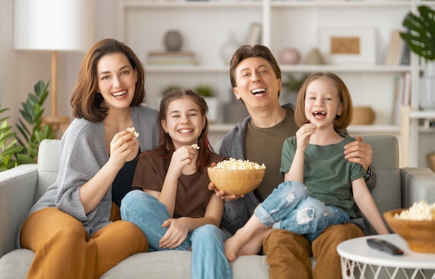 Famille heureuse regardant des films télévisés sur projecteur avec du pop-corn le soir à la maison