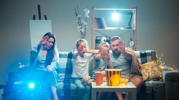 Famille heureuse regardant un projecteur, une télévision, des films avec du pop-corn le soir à la maison.