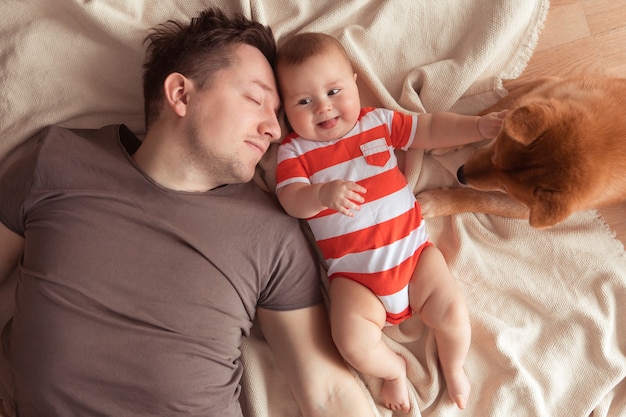 Famille heureuse s'amusant avec un mignon chien Shiba Inu. Père avec son bébé souriant et son animal de compagnie Shiba Inu à la maison, vue de dessus