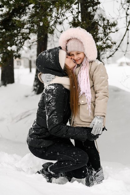 Une famille heureuse s'amuse dans la forêt d'hiver. Mère et fille se câlinant et jouant avec la neige. Notion de famille. Profiter de passer du temps ensemble