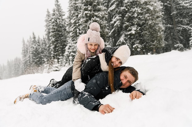 Une famille heureuse s'amuse dans la forêt d'hiver. Mère, père et fille sont allongés sur le sol et jouent avec la neige. Notion de famille. Profiter de passer du temps ensemble
