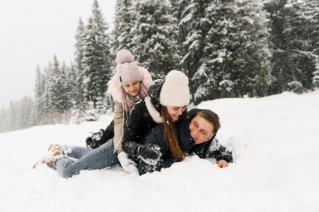 Une famille heureuse s'amuse dans la forêt d'hiver. Mère, père et fille sont allongés sur le sol et jouent avec la neige. Notion de famille. Profiter de passer du temps ensemble