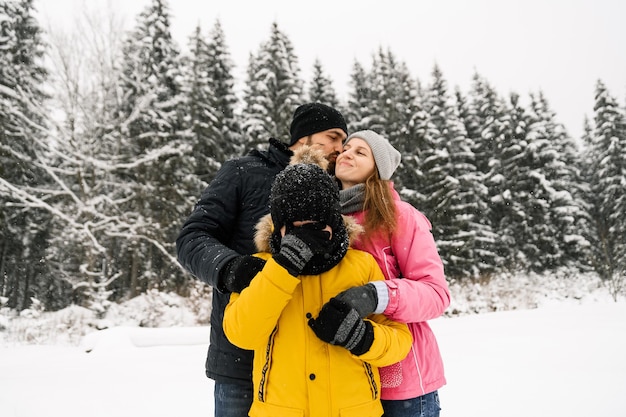 Une famille heureuse s'amuse dans la forêt d'hiver et regarde la caméra. Mère, père et fils jouant avec la neige. Notion de Noël en famille. Profiter de passer du temps ensemble