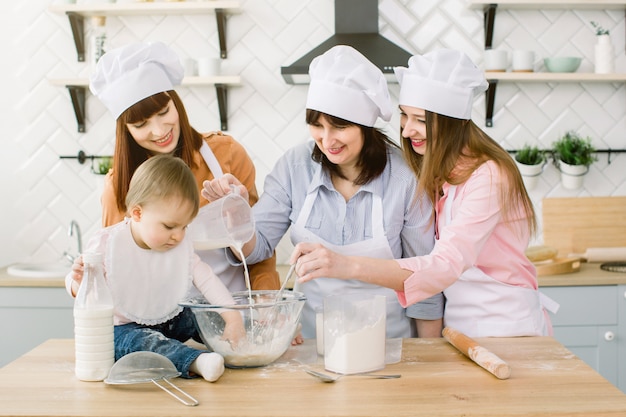 Famille heureuse, s'amuser dans la cuisine. Grand-mère et ses filles et petite fille pétrir la pâte ensemble dans la cuisine à la maison. Bonne fête des mères, cuisine familiale