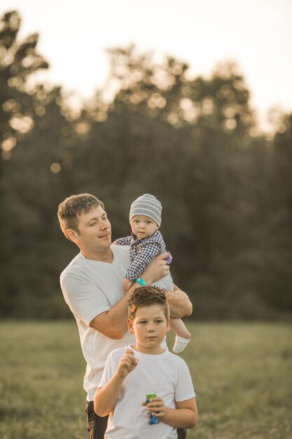 Famille heureuse s'embrassant et s'embrassant lors d'une promenade d'été Père et ses deux fils marchant dans le parc et profitant de la belle nature Portrait de famille mignon