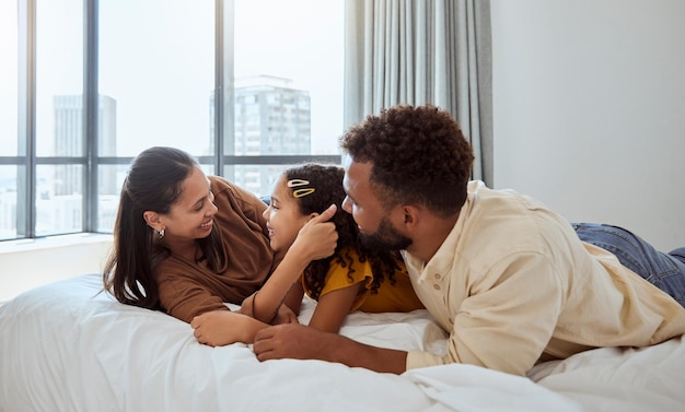 Une famille heureuse se détend et une fille au lit avec la mère et le père se lie et se repose dans leur maison ensemble Aime la famille noire et l'enfant profite d'une matinée paresseuse à l'intérieur avec les parents se reposent et s'embrassent dans la chambre