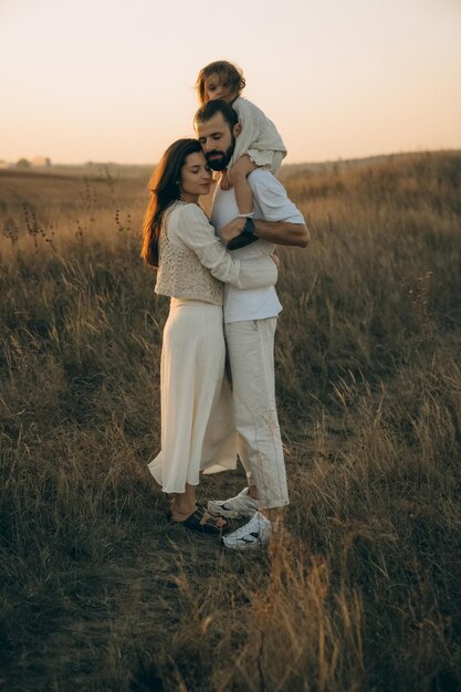 Une famille heureuse se promène dans la nature, tous ensemble, une mère joyeuse, un père barbu et une petite fille se promènent sur les pentes par une belle soirée d'été.