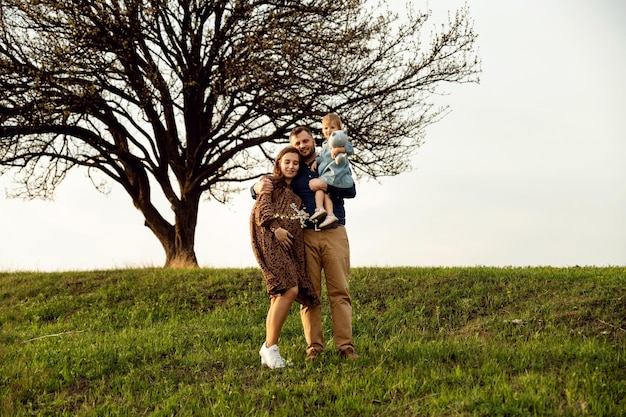 Famille heureuse se promène sur l'herbe de printemps femme enceinte avec petite fille et mari promenade en famille au coucher du soleil famille internationale futurs parents ventre de femme enceinte