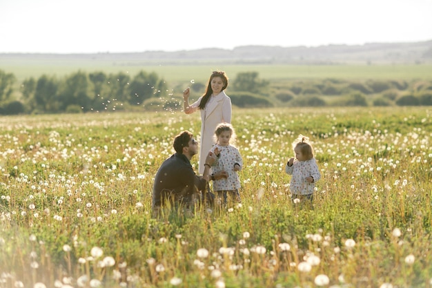 Une famille heureuse se promène sur le terrain et joue avec les pissenlits.