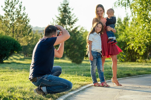 Une famille heureuse se repose dans le parc en été. belle mère, beau père avec un petit garçon et une jolie fille photographiée à la caméra. séance photo de famille photographe masculin