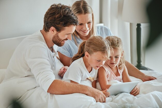 Famille heureuse et tablette pour se divertir sur le lit en regardant des émissions ensemble tout en se relaxant à la maison Mère, père et enfants se détendent avec le sourire pour une diffusion en ligne sur écran tactile dans la chambre