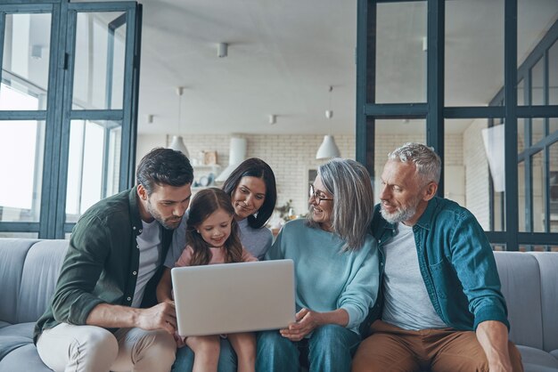 Famille heureuse utilisant un ordinateur portable et souriant tout en passant du temps à la maison ensemble