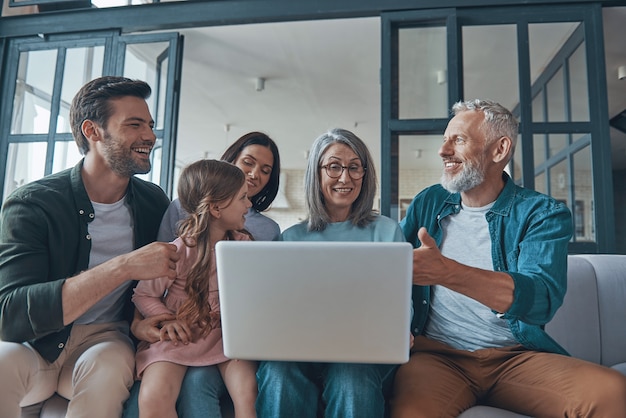 Famille heureuse utilisant un ordinateur portable et souriant tout en passant du temps à la maison ensemble