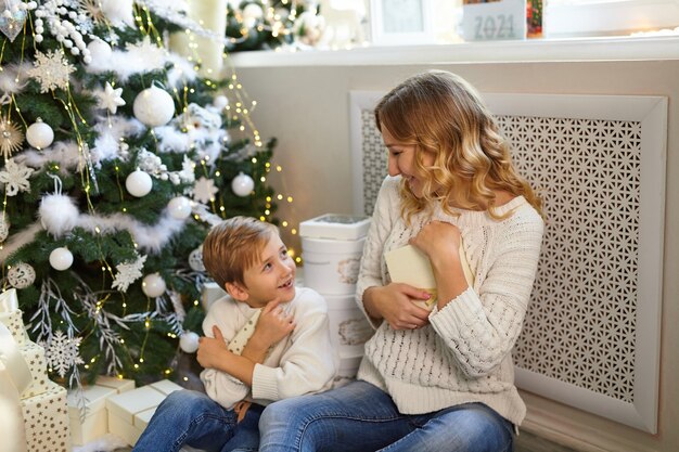 Famille heureuse en vacances, mère et son mignon petit garçon, ils se félicitent au cadeau de Noël sous le sapin de Noël