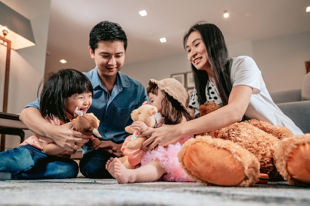 Famille heureuseLes parents jouent avec des ours en peluche et des jouets avec leurs enfants assis sur le tapis dans le salon à la maisonActivité de week-end concept de mode de vie familial heureux