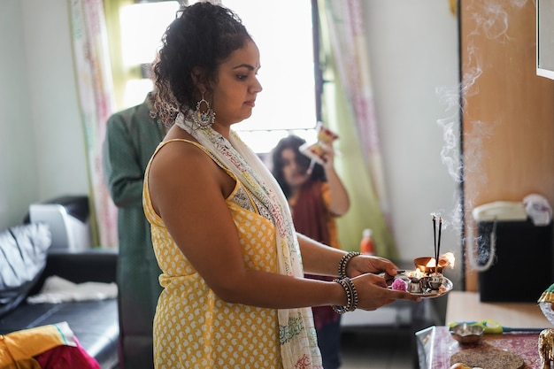 Famille indienne célébrant Diwali ou festival hindou à la maison - Focus sur les mains de la mère tenant des offrandes