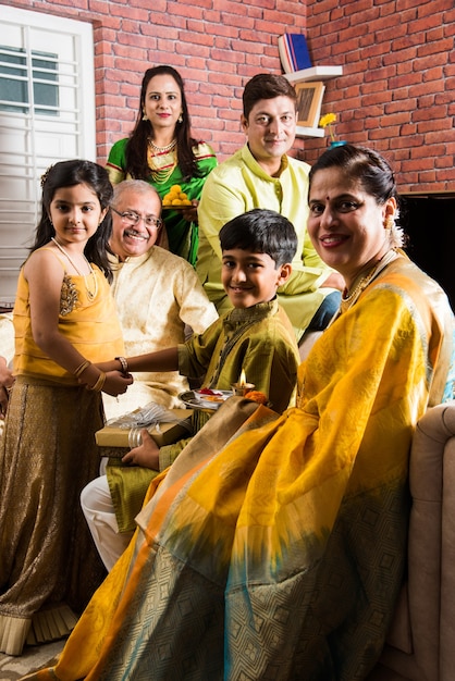 Famille indienne célébrant le festival Raksha Bandhan ou Rakhi à la maison tout en portant des vêtements traditionnels et assis sur un canapé