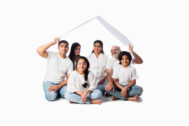 Famille indienne et concept immobilier - Famille asiatique multigénérationnelle tenant un modèle de maison en papier avec des clés contre un mur blanc