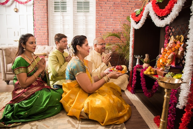 Famille intelligente asiatique indienne exécutant Ganesh puja ou Aarti à la maison tout en portant des vêtements traditionnels