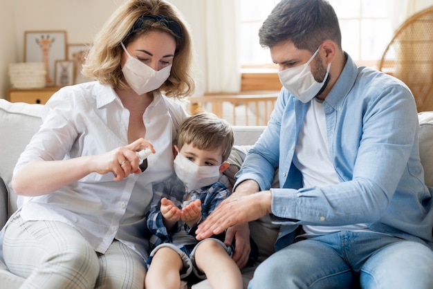 Photo famille à l'intérieur utilisant un désinfectant et portant des masques médicaux